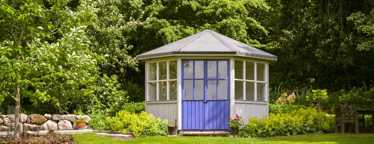 A timber summerhouse with a purple door in a planted garden